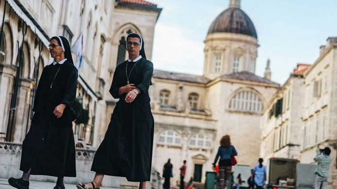 Two Catholic Nuns walking across city place, church in the background