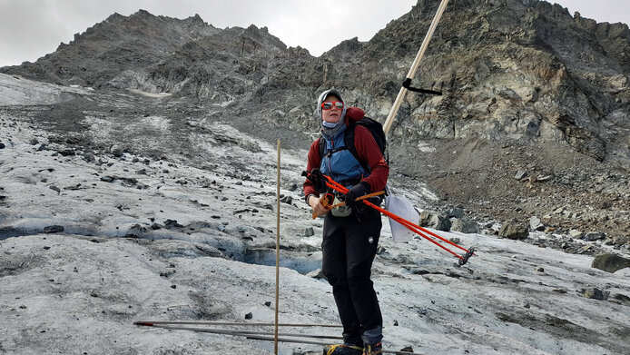 Forscherin auf einem Gletscher mit wenig Schnee, im Hintergrund viel Geröll und Steine