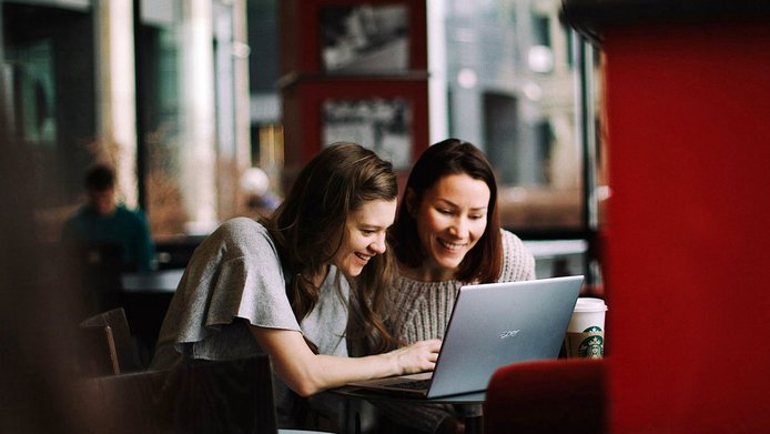Zwei junge Frauen beugen sich über einen Laptop in einem Café