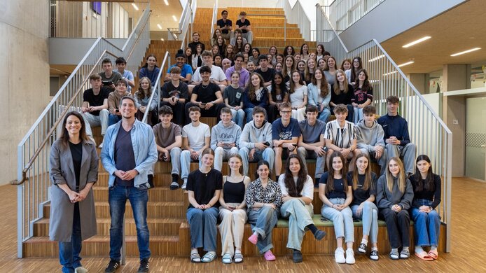 Gruppenbild einer Schulklasse mit Lehrer und Journalistin im Stiegenhaus des Schulgebäudes
