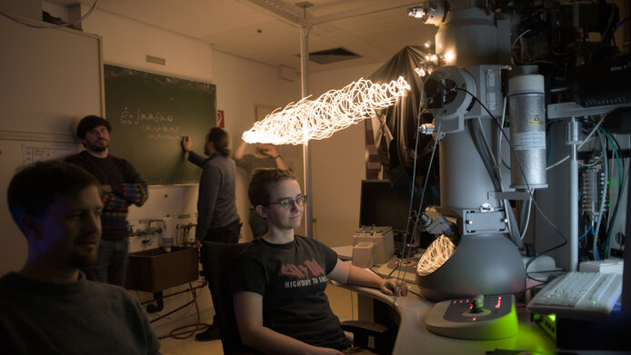 Young team of quantum physicists in the lab with a large microscope and fairy lights