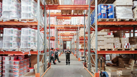 Young warehouse worker in uniform moves between very high shelves.