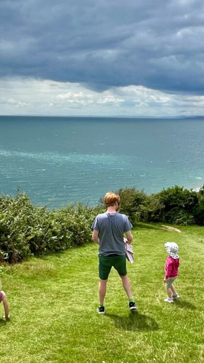 Vater mit zwei kleinen Kindern auf Wiese vor einer Küste