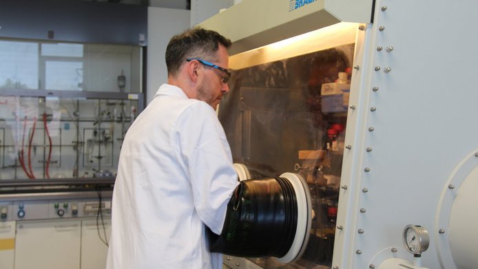 A young researcher in a white lab coat in the lab—his hands are inside a hermetically sealed reactor.