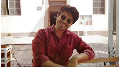 Porträt eines jungen Forschenden mit Sonnenbrille und rotem Hemd auf einem Platz im Freien