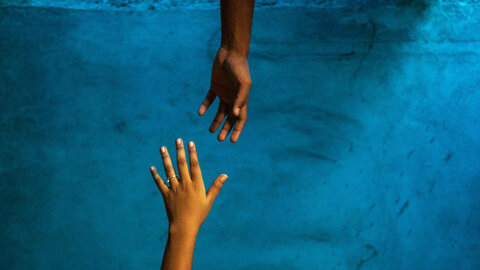 A helping hand reaches out to an outstretched hand against a dark background.
