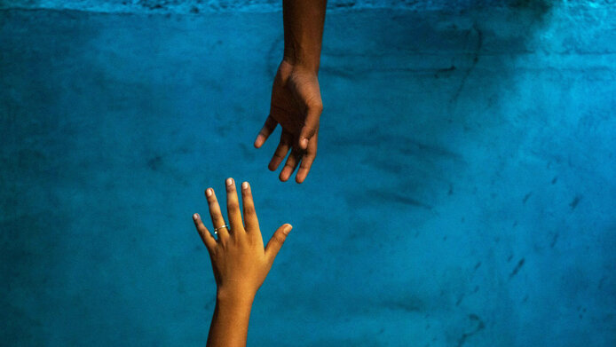 A helping hand reaches out to an outstretched hand against a dark background.