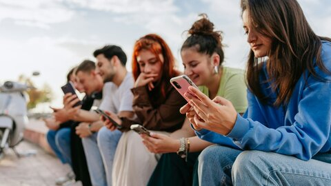 junge Menschen sitzen am Straßenrand und scrollen durch die Sozialen Medien auf ihren Handys