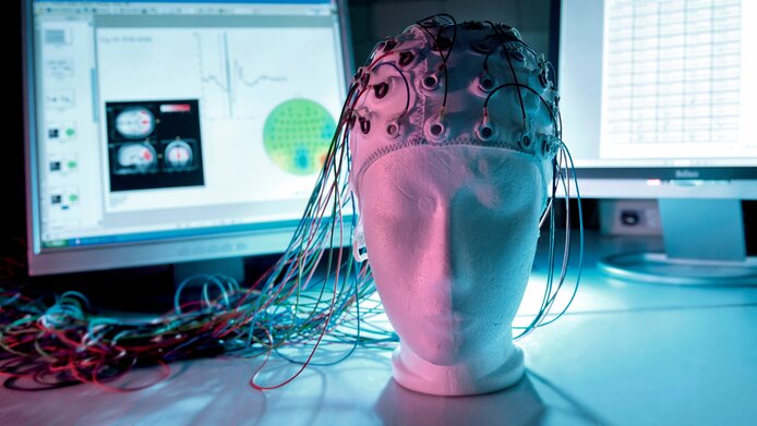Plaster head with a helmet equipped with electrodes for measuring brain waves, screen recordings in the background