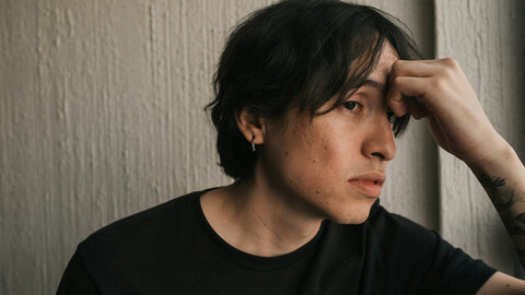 Young man in a black T-shirt, head propped up on his arm, looking sad