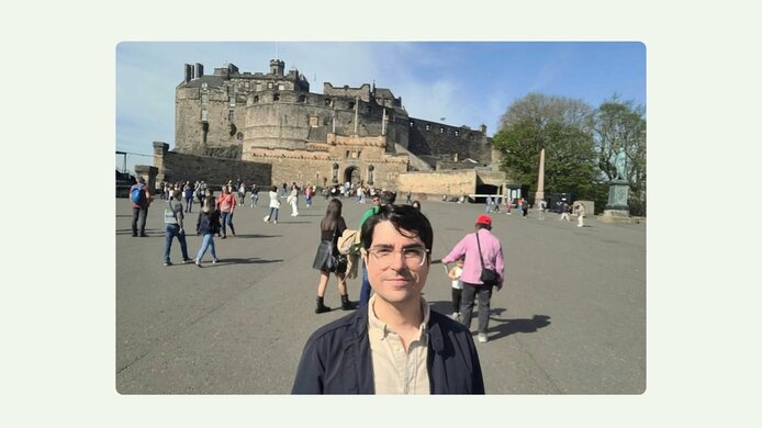 A young man with glasses and dark hair in front of Edinburgh Castle