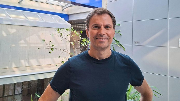 Forscher mit blauem T-Shirt steht vor einem Institutsgebäude 