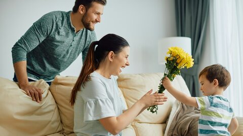 Happy mother receiving a bouquet of yellow flowers from her young son at home