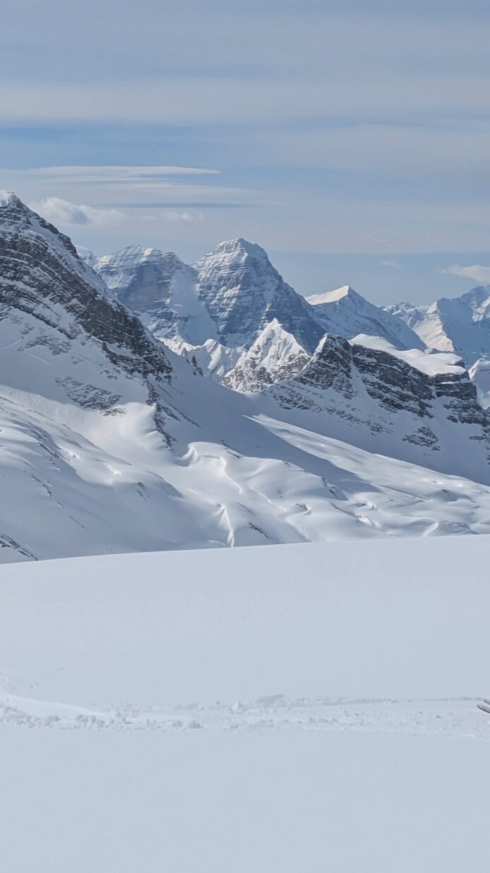 Schneebedeckte Berge mit Frau auf Skitour im Vordergrund. 