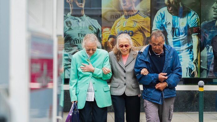 Old people smiling and walking along the road supporting each other.