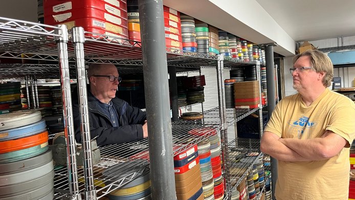 Two people in a film archive filled with countless reels of film