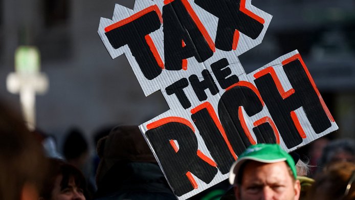 Ein Demonstrant hält bei einer Protestkundgebung gegen Rentenkürzungen und Arbeitsmarktreformen ein Plakat mit der Aufschrift „Besteuert die Reichen“ hoch