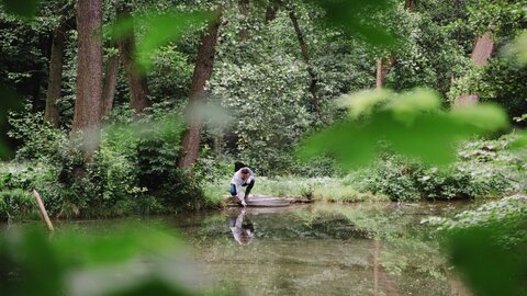 A male researcher takes a water sample from a bog in the forest
