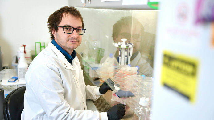 Young male researcher with white lab coat, brown hair and glasses in the lab