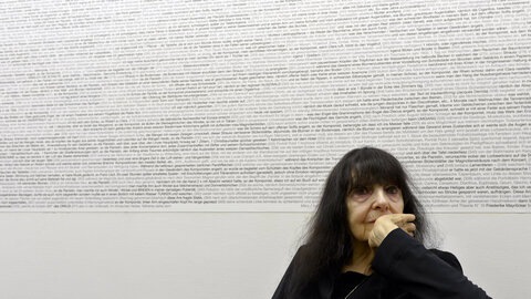 Black and white photograph of the writer Friederike Mayröcker at the age of 90 in front of a wall of words