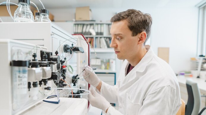 A young researcher in a white lab coat in a chemistry lab