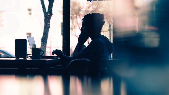 Junger Mann mit Mütze sitzt in einem Kaffehaus vor dem Laptop und arbeitet.