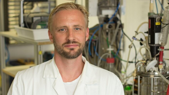 Young researcher with short blond hair and beard, white coat, in the lab