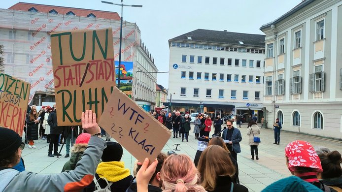 Protesters hold up cardboard signs in the town square in front of City Hall 