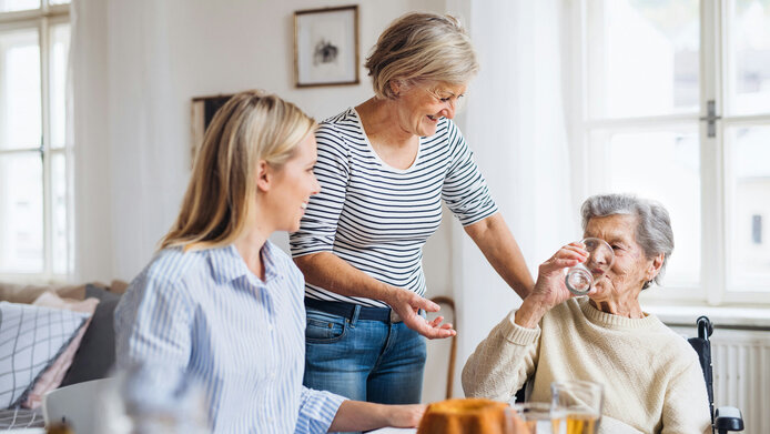 Happy elderly woman in wheelchair with family sitting at table and drinking at home