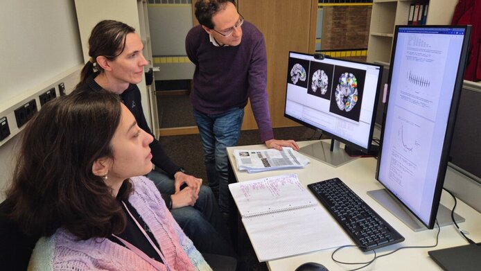 A research team of two women and one man look at brain scans on the computer