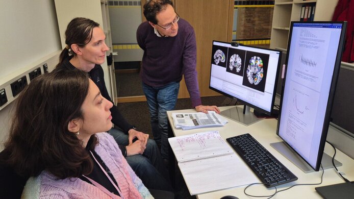 Ein Forscherteam aus zwei Frauen und einem Mann blicken auf Gehirnscans am Computer