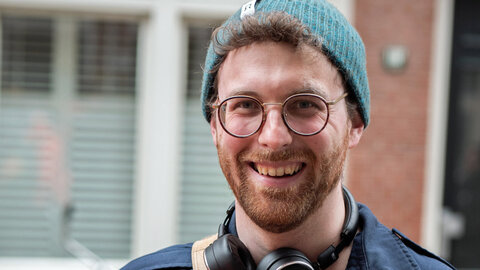 Portrait eines jungen Wissenschaflters mit rotem Bart, Brille und Strickmütze in Petrol