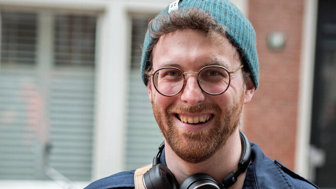 Portrait of a young scientist with a red beard, glasses and knitted cap in petrol