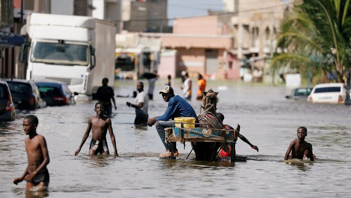 Überflutete Straße in Dakar, Westafrika - Menschen waten durch Wasser, das bis zum Nabel reicht