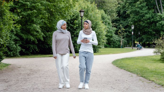 Two young Muslim women are walking in a park in an urban setting