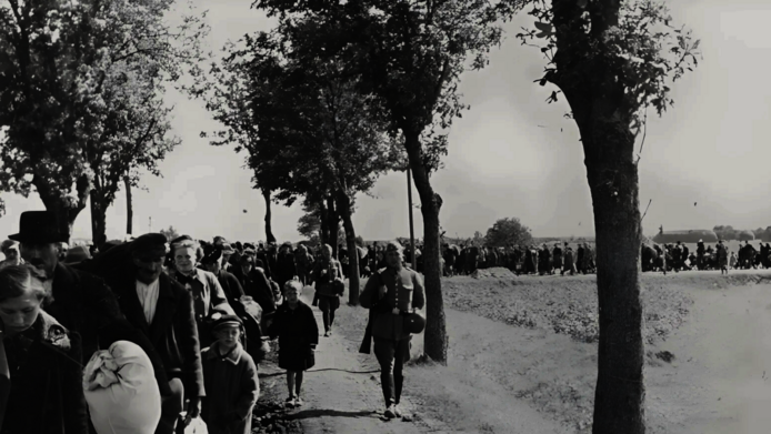 1939, black-and-white photo: a long line of people marching down an avenue toward the train station: families, children, adults being forcibly resettled in Poland