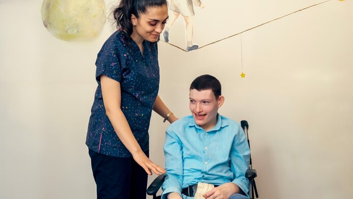 A young person in a wheelchair with physical and mental disabilities is being treated by a doctor.