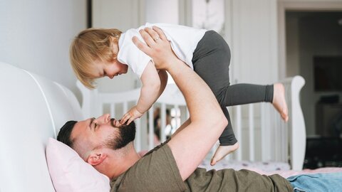 Vater auf dem Sofa hebt seine Kleine Tochter hoch 