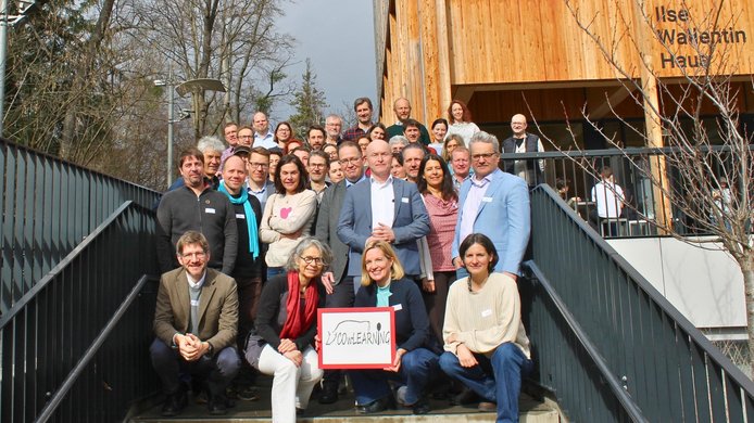 Group photo of 30 experts from the fields of science and agriculture on the steps leading up to the entrance of a wooden building