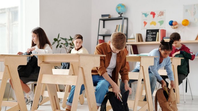 Junge Schüler:innen im Klassenzimmer packen ihre Rucksäcke ein