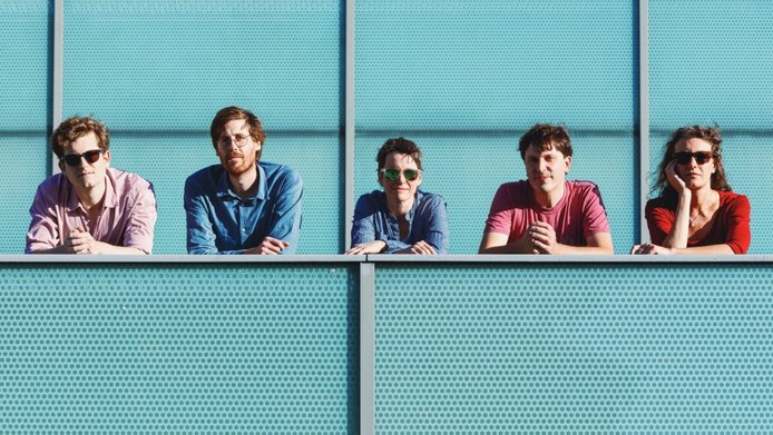 Zwei weibliche und drei männliche Musiker:innen lehnen an einem Geländer und schauen in die Kamera