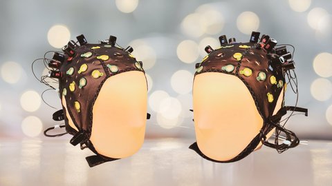 Zwei beleuchtete Kopfpuppen sind aufeinander gerichtet und haben EEG-Mützen auf, um ihre Gehirnaktivität zu messen. 