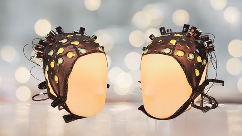 Two illuminated head mannequins are facing each other and are wearing EEG caps to measure their brain activity.
