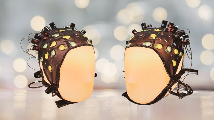 Zwei beleuchtete Kopfpuppen sind aufeinander gerichtet und haben EEG-Mützen auf, um ihre Gehirnaktivität zu messen. 