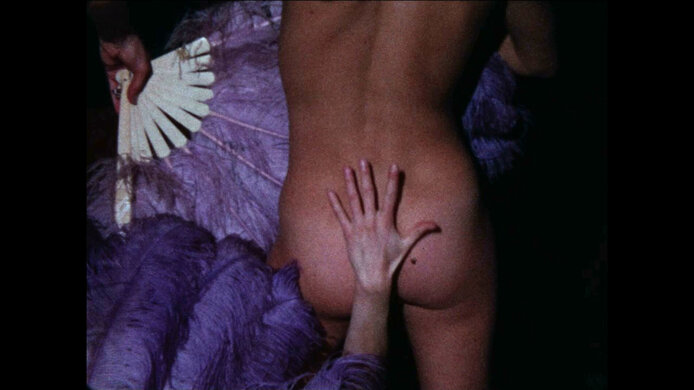 Queer film still: female hand lies on a man's naked buttocks. 