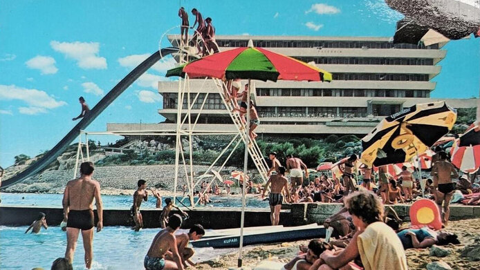 Menschen am Strand mit riesigem Hotelgebäude im Hintergrund aus der Zeit des Kalten Krieges