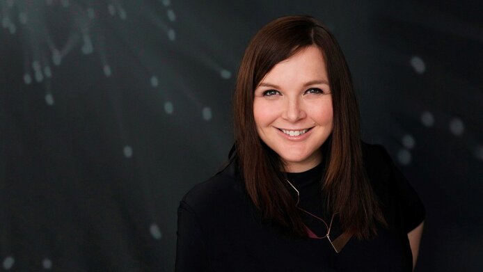 Portrait of a young researcher with half-length dark brown hair against a dark background.