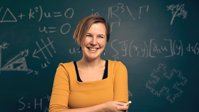 Young woman with orange T-Shirt and chalk in the hand in front of a blackboart with mathematical formulas