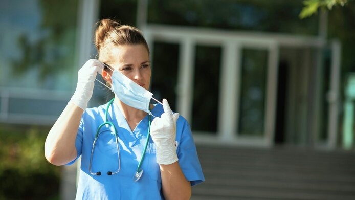 Ärztin vor dem Krankenhaus, nimmt sich die Schutzmaske vom Gesicht