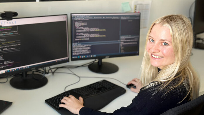 Junge Frau mit langen blonden Haaren vor zwei Computerbildschirmen 